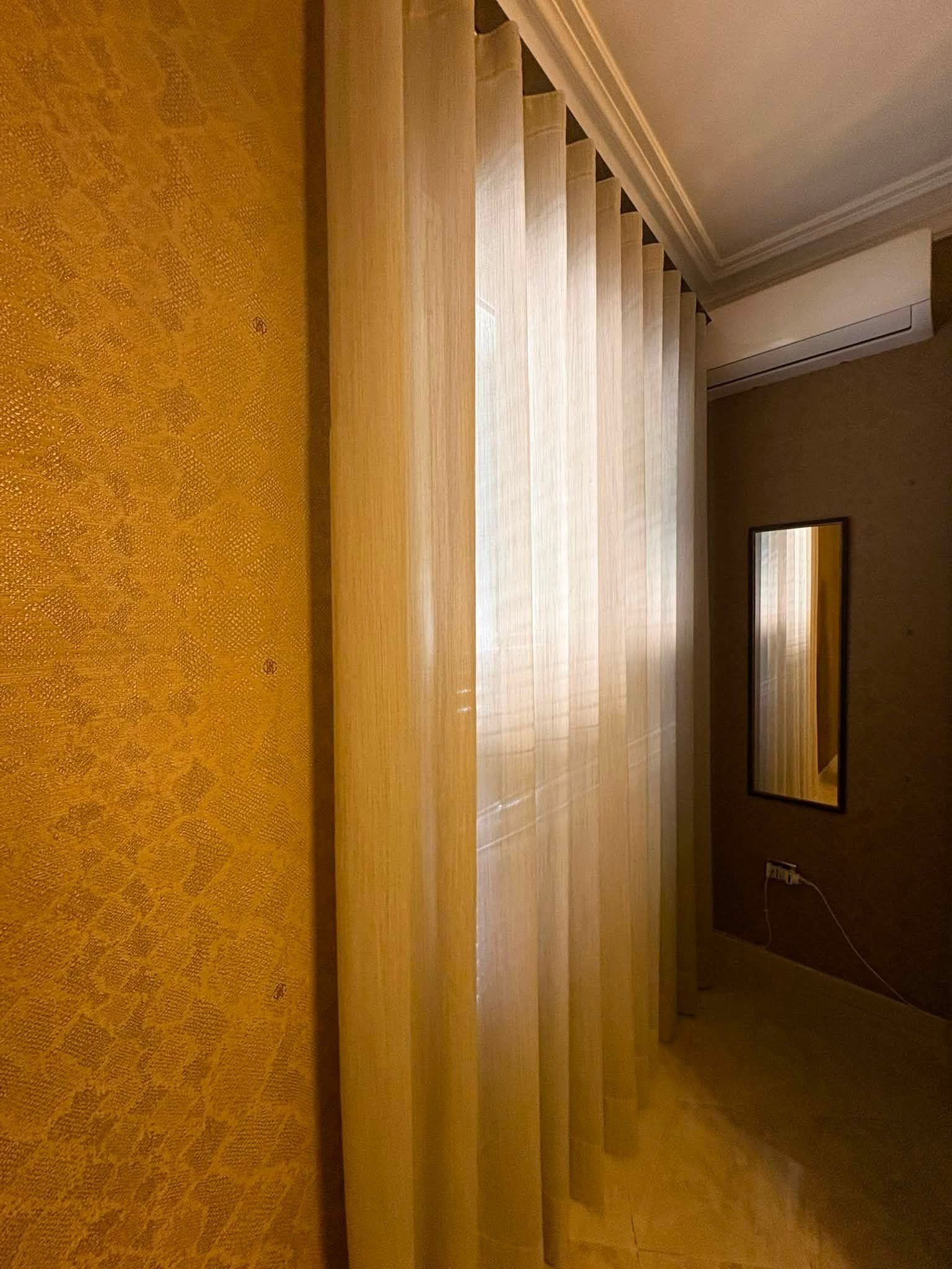 Stretto corridoio con tende trasparenti, uno specchio a parete e pareti color beige caldo illuminate da una luce soffusa.