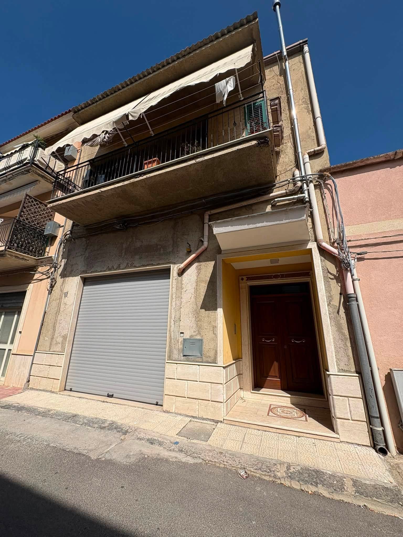 Vista ravvicinata di un edificio beige a due piani con balconi e una porta con serranda metallica chiusa.