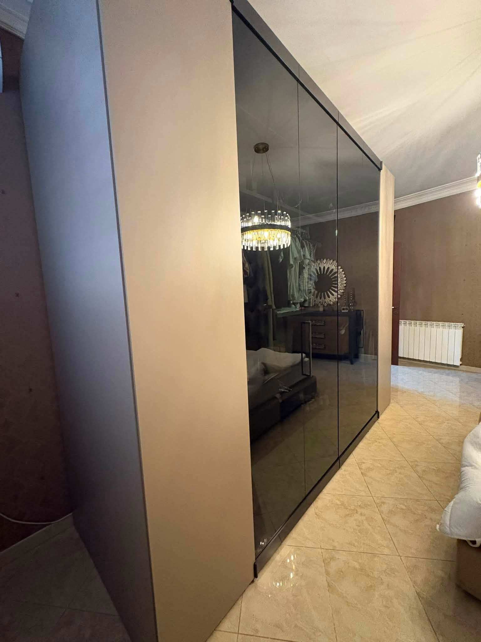 Camera da letto moderna con un alto armadio a specchio accanto al letto e il riflesso del lampadario.