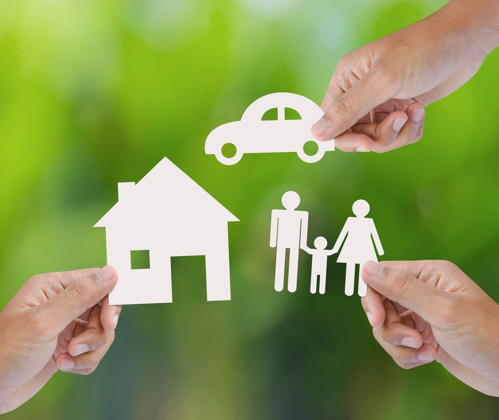 Mani che reggono icone di carta raffiguranti una casa, un'auto e una famiglia, su uno sfondo verde sfocato.