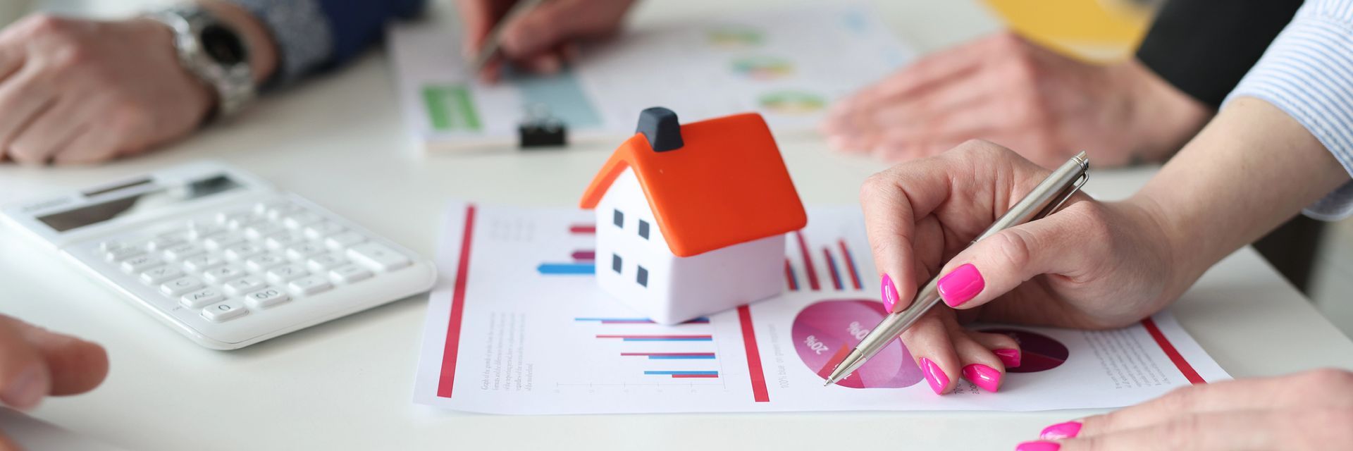 Mani che disegnano il modello di una casa e dei grafici a una scrivania con calcolatrice e fogli di carta.