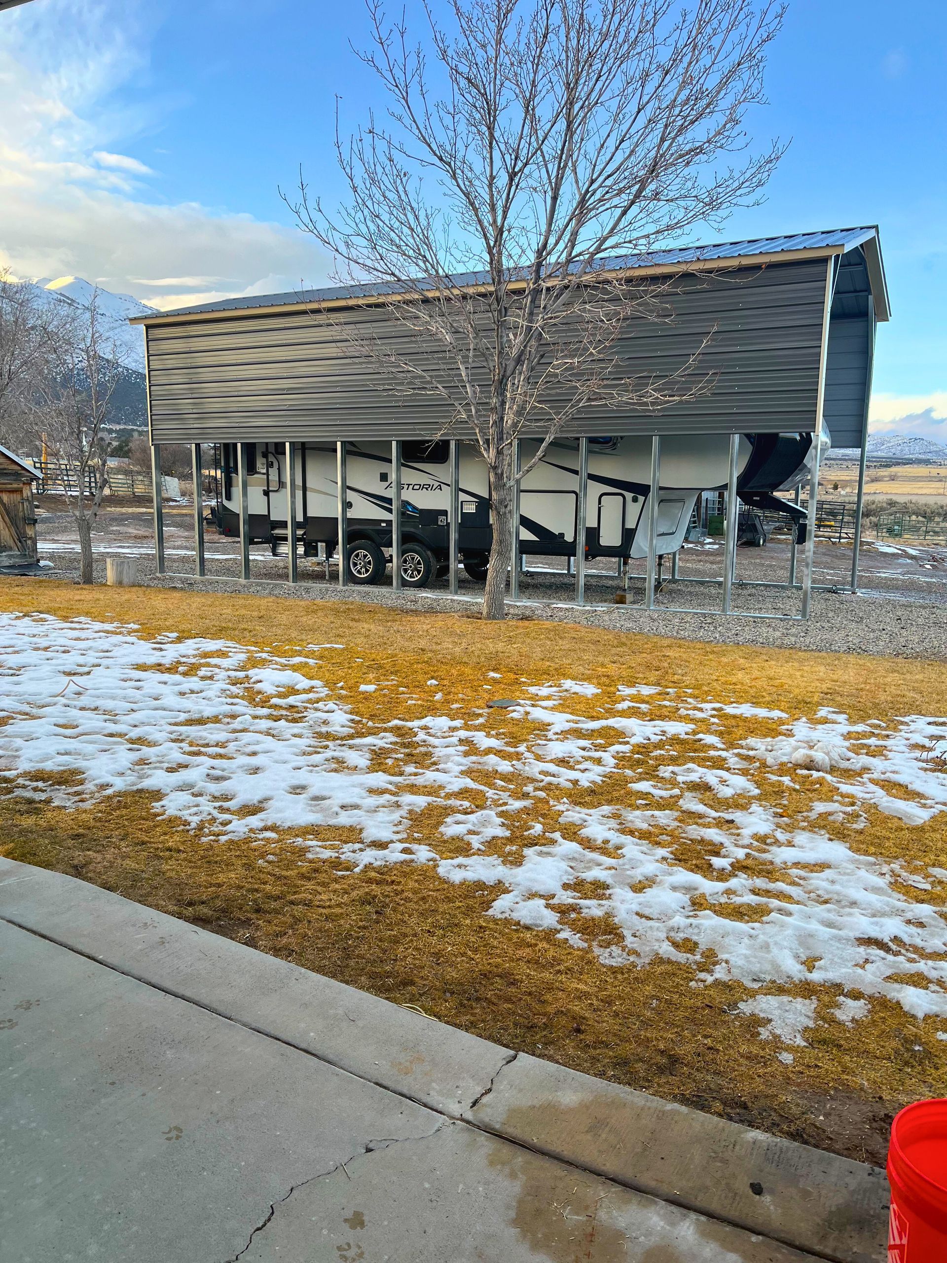 A trailer is parked under a shed in the snow.