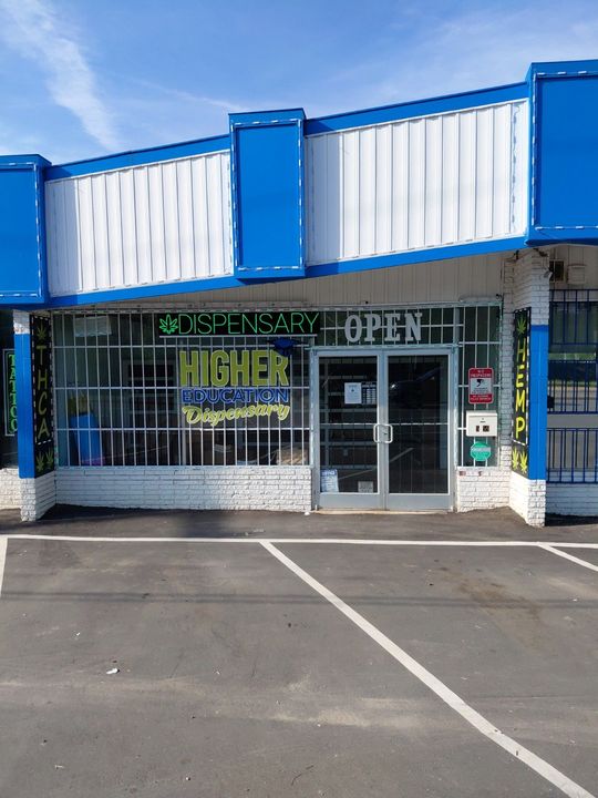 Storefront with blue trim, barred windows, and an “OPEN” sign in a small parking lot.