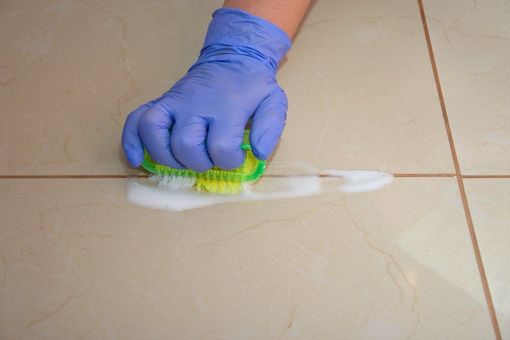 A Person Wearing Gloves Is Cleaning a Tile Floor with A Sponge — Turbo Clean in Tuncurry, NSW