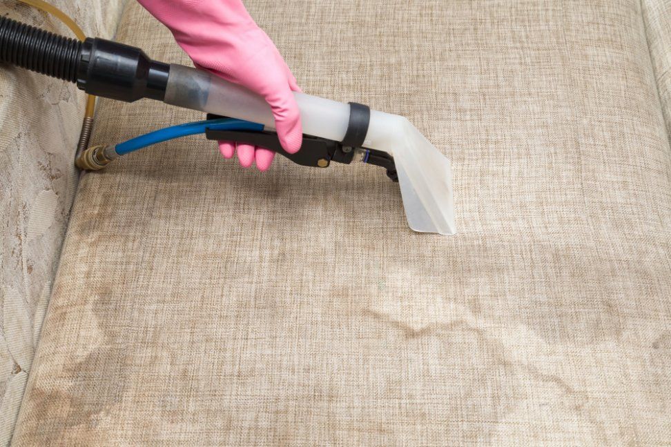 A Person Is Cleaning a Couch with A Vacuum Cleaner — Turbo Clean in Hallidays Point, NSW