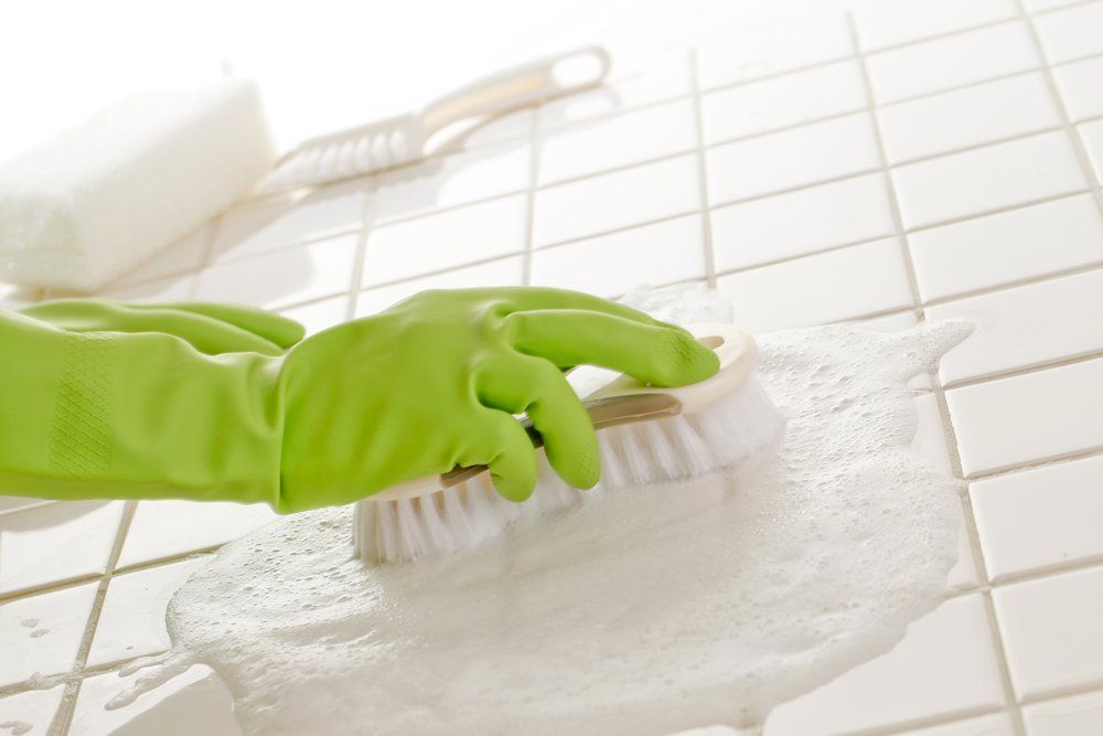 A Person Wearing Green Gloves Is Cleaning a Tile Floor with A Brush — Turbo Clean in Forster, NSW