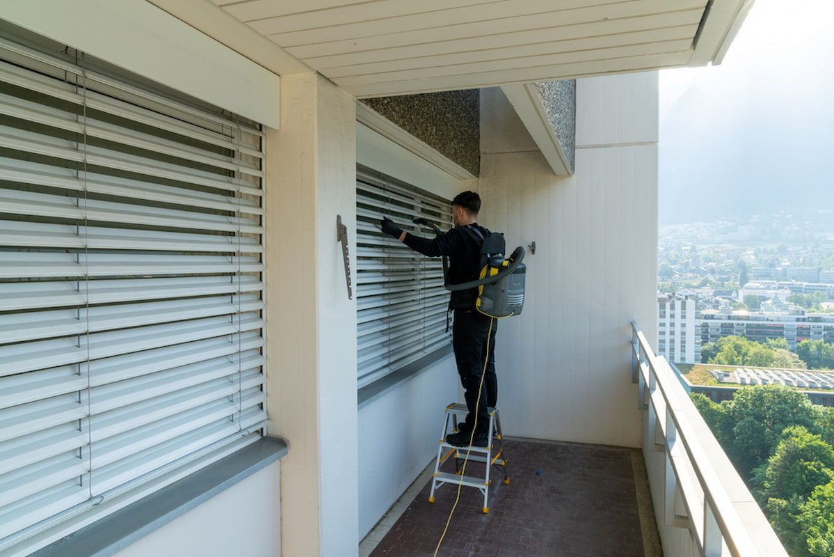A Man Is Standing on A Ladder Cleaning Blinds on A Balcony — Turbo Clean in Taree, NSW