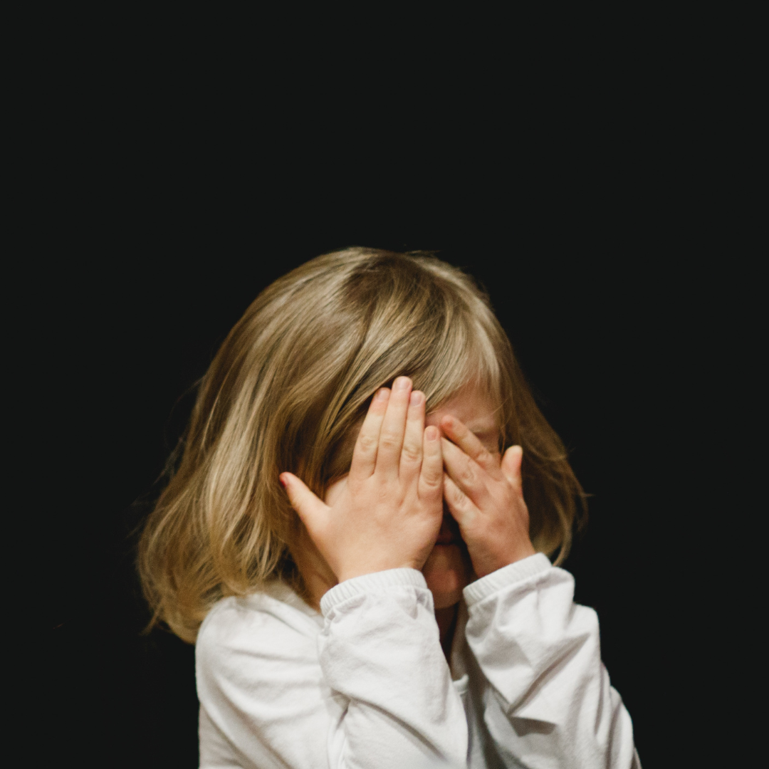 A little girl is covering her eyes with her hands.