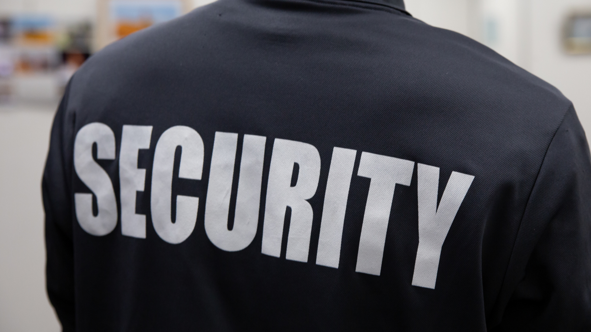 A security guard is wearing a black jacket with the word security on the back