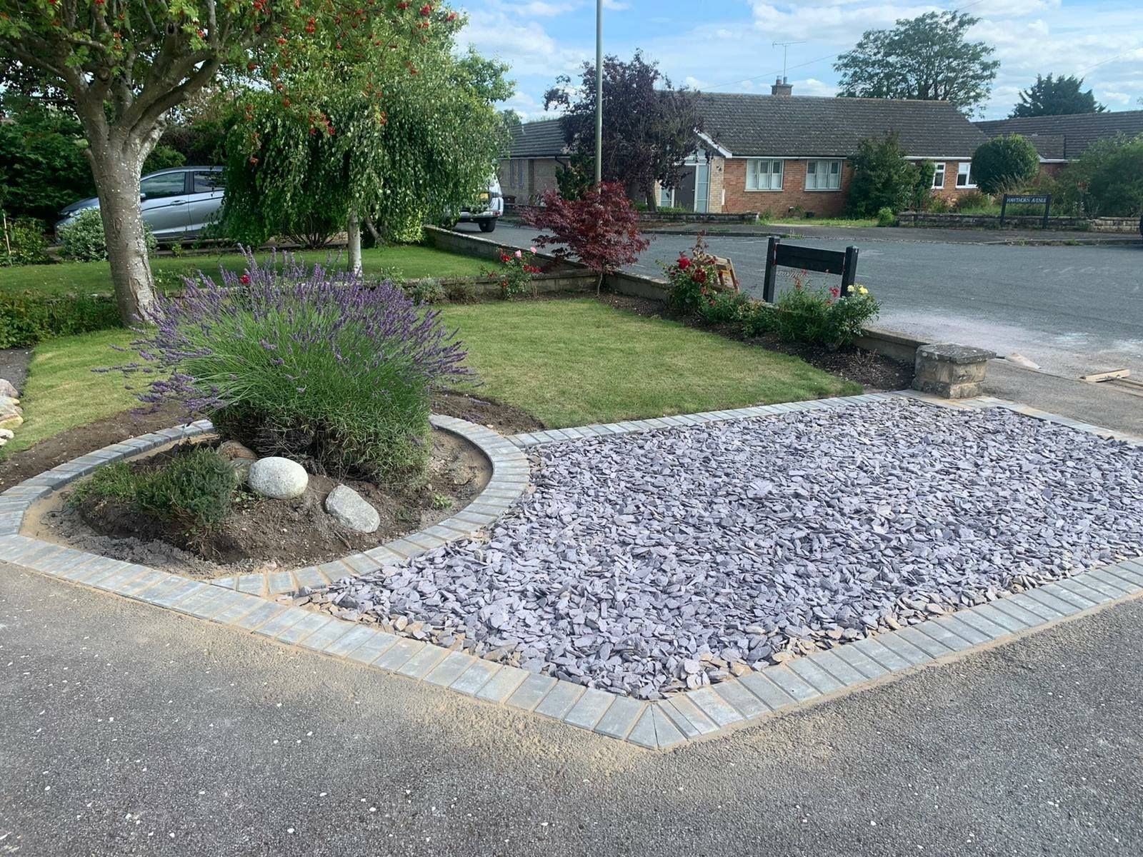 Front yard landscaping with purple flowers, rocks, and a gravel bed beside a residential street