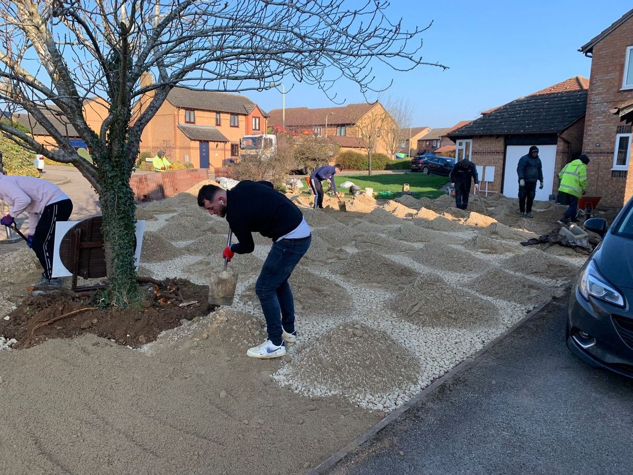 People landscaping a gravel yard beside houses on a sunny day