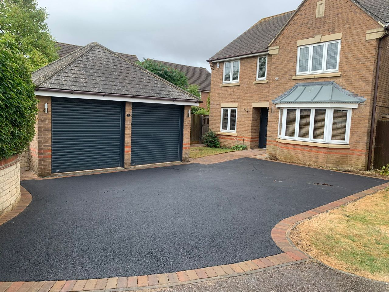 Brick house with double garage and fresh black driveway in a suburban driveway.