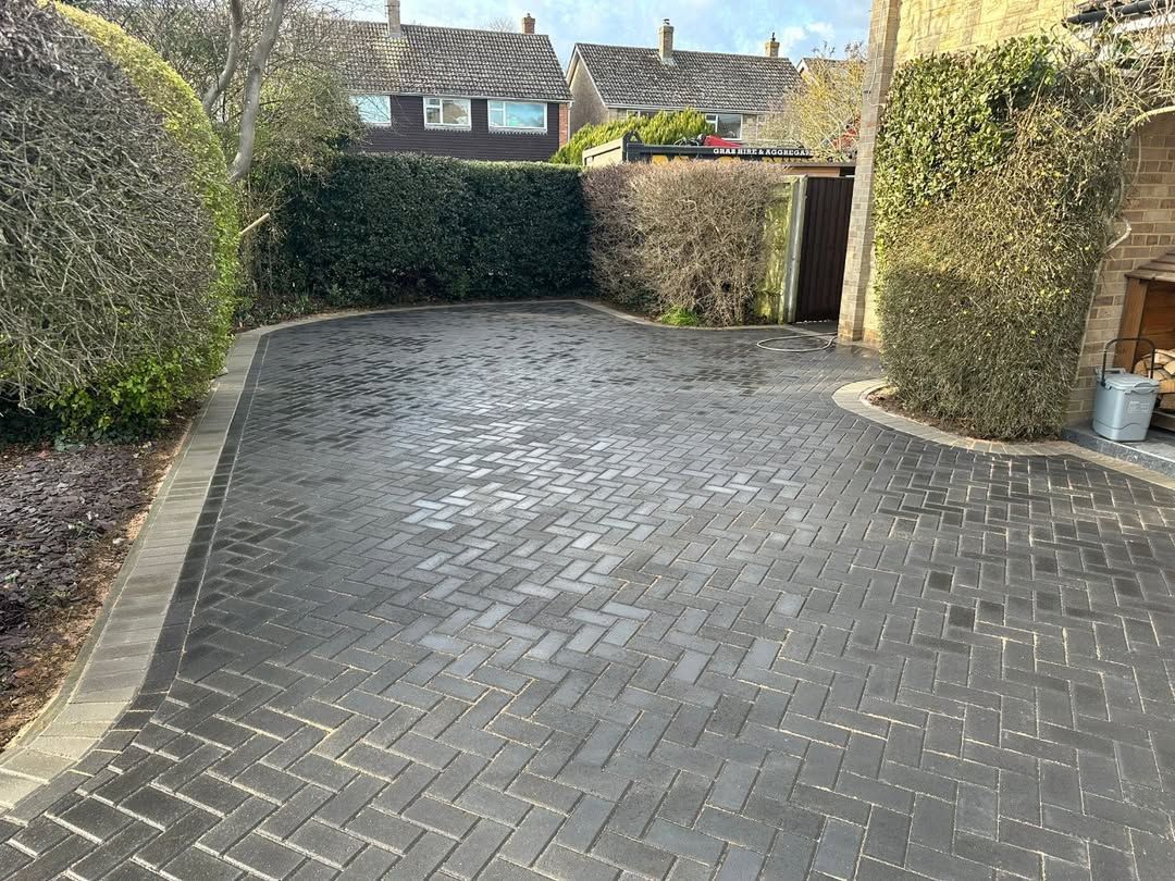 Brick-paved driveway with hedges and stone houses in the background