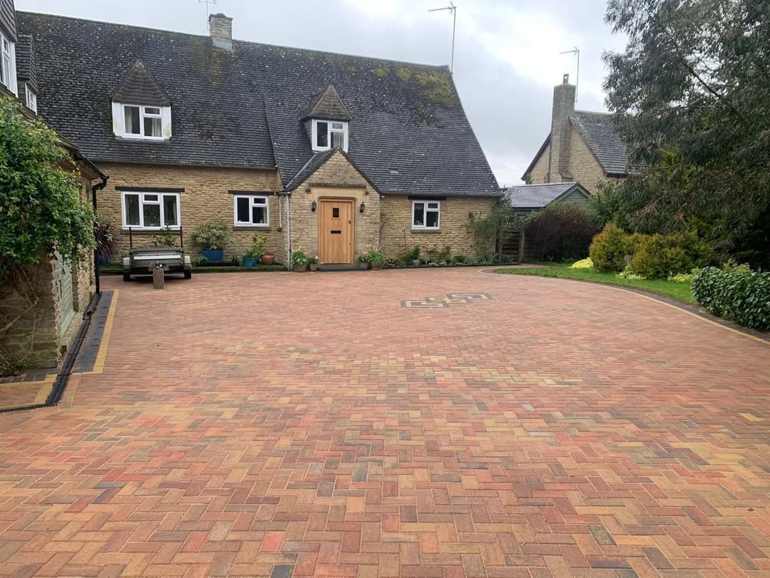 Stone cottage with large brick-paved driveway and slate roof under cloudy sky