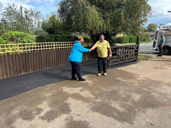 Two people shaking hands beside a fence and trees on a sunny outdoor path