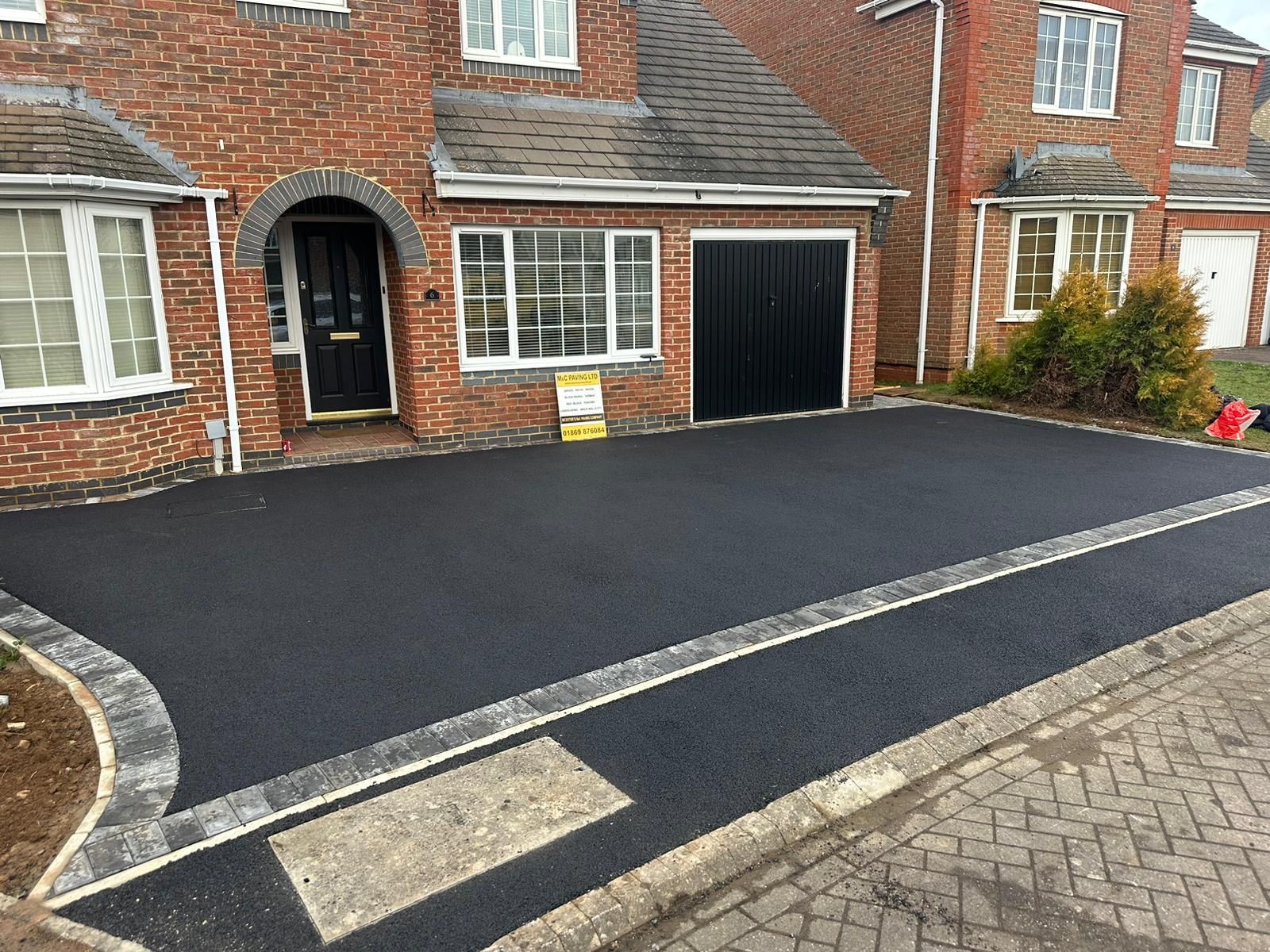 Freshly paved black driveway in front of a brick house with a black garage door and front entrance