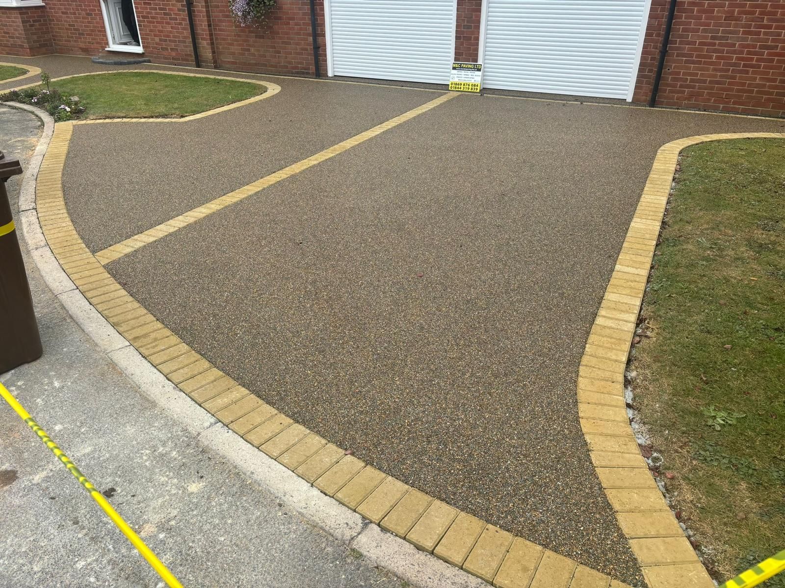 Gravel driveway with yellow brick border leading to white garage doors beside a brick house