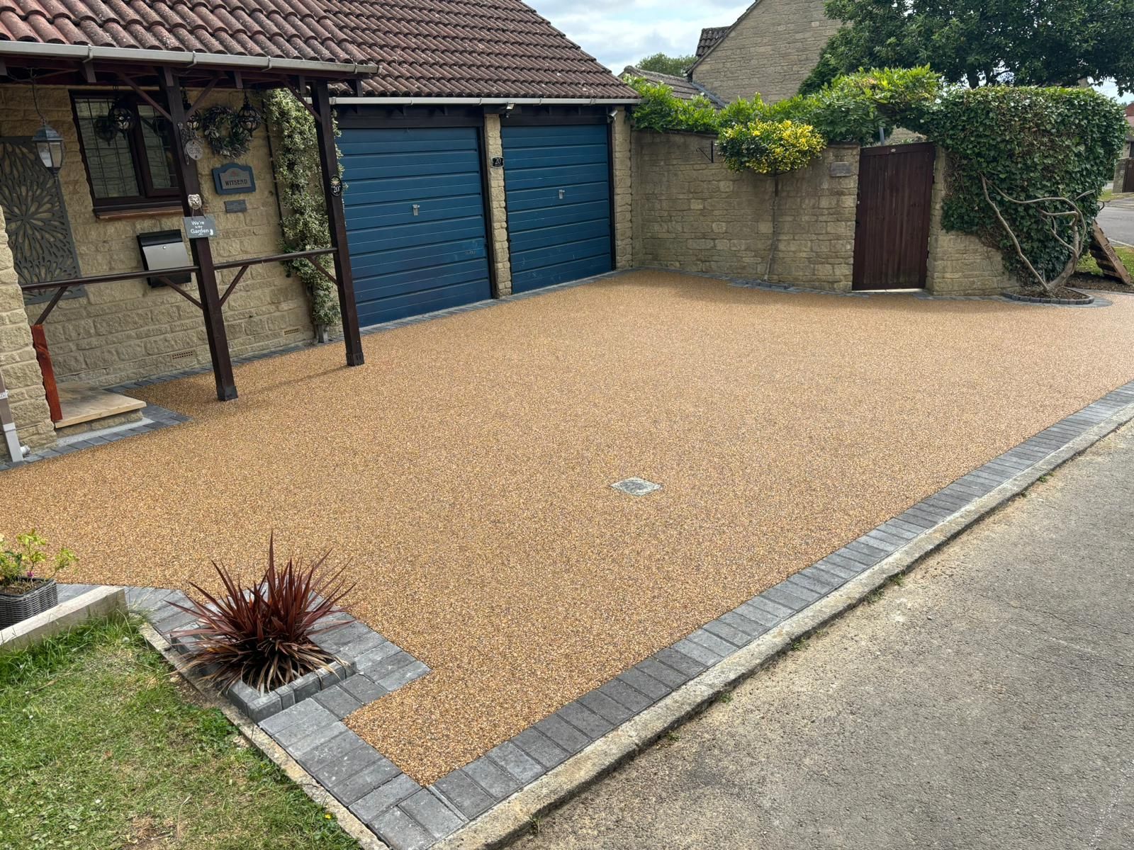 Gravel driveway bordered by gray pavers, with blue garage doors and a house entrance beside it.