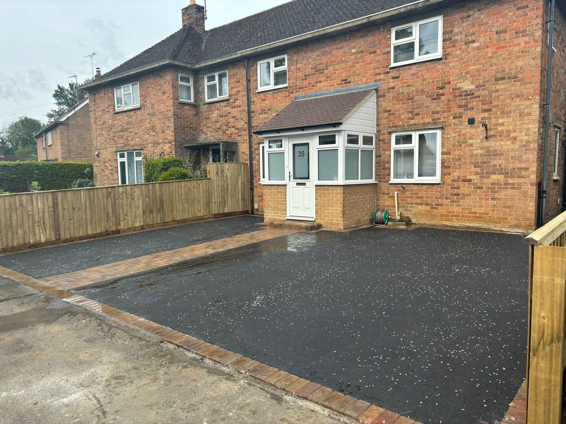 Brick house with a paved driveway and wooden fencing in the front yard.