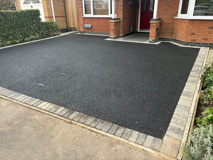 Freshly paved black driveway in front of a brick house with light stone edging, viewed from the street