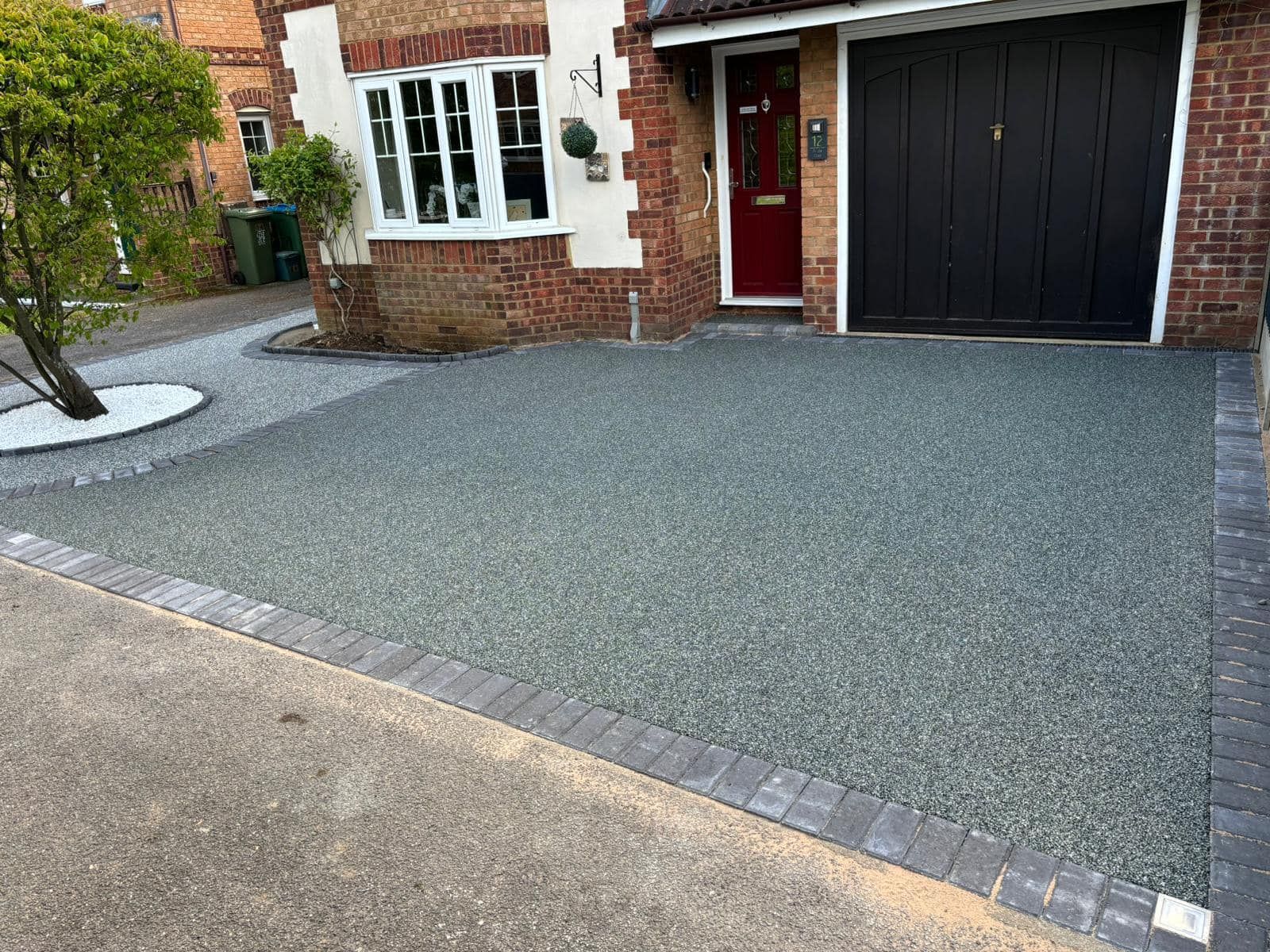 Freshly paved gray driveway beside a brick house with a black garage door and red front door