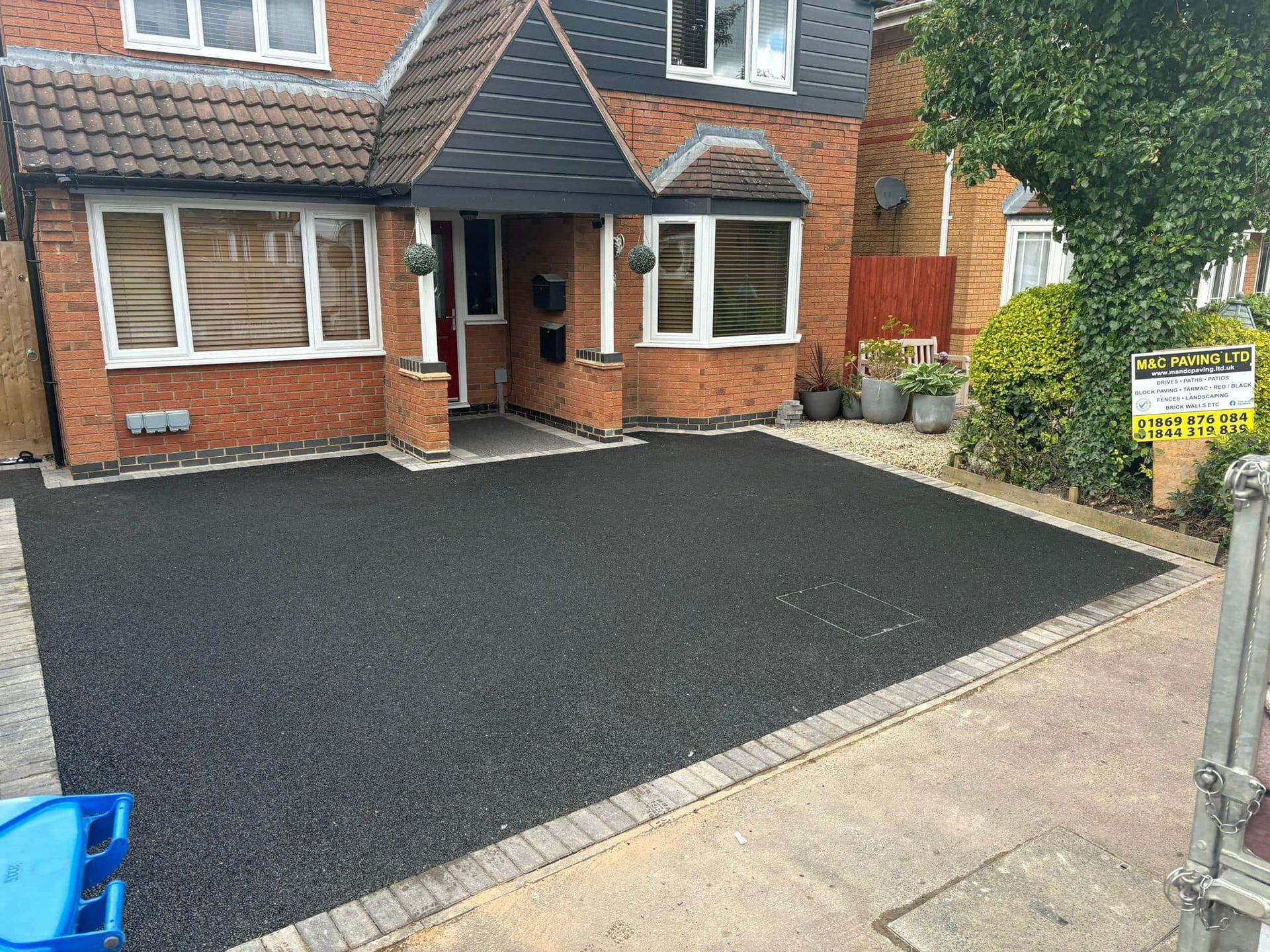 Brick house with fresh black driveway and front garden, viewed from the street