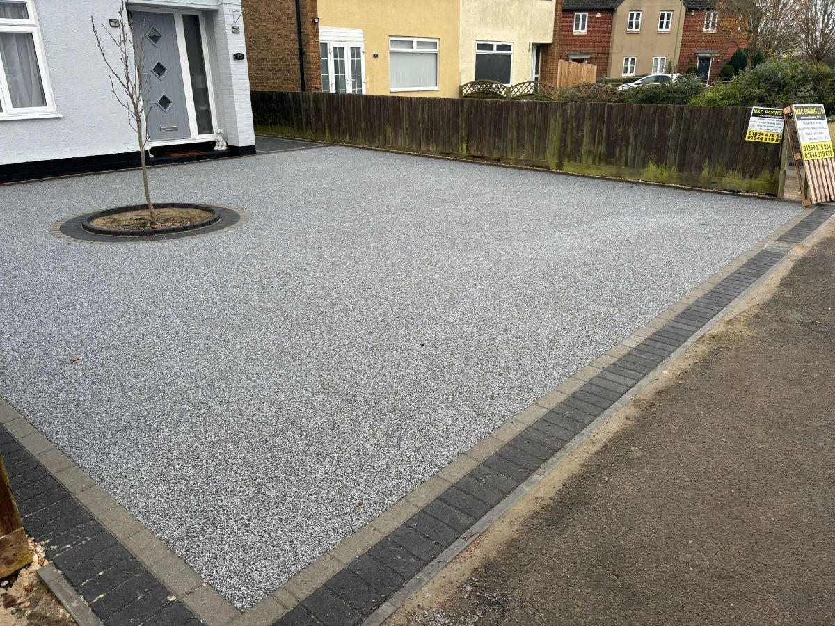 Gravel-covered courtyard bordered by pavement, with a small tree and apartment buildings in the background
