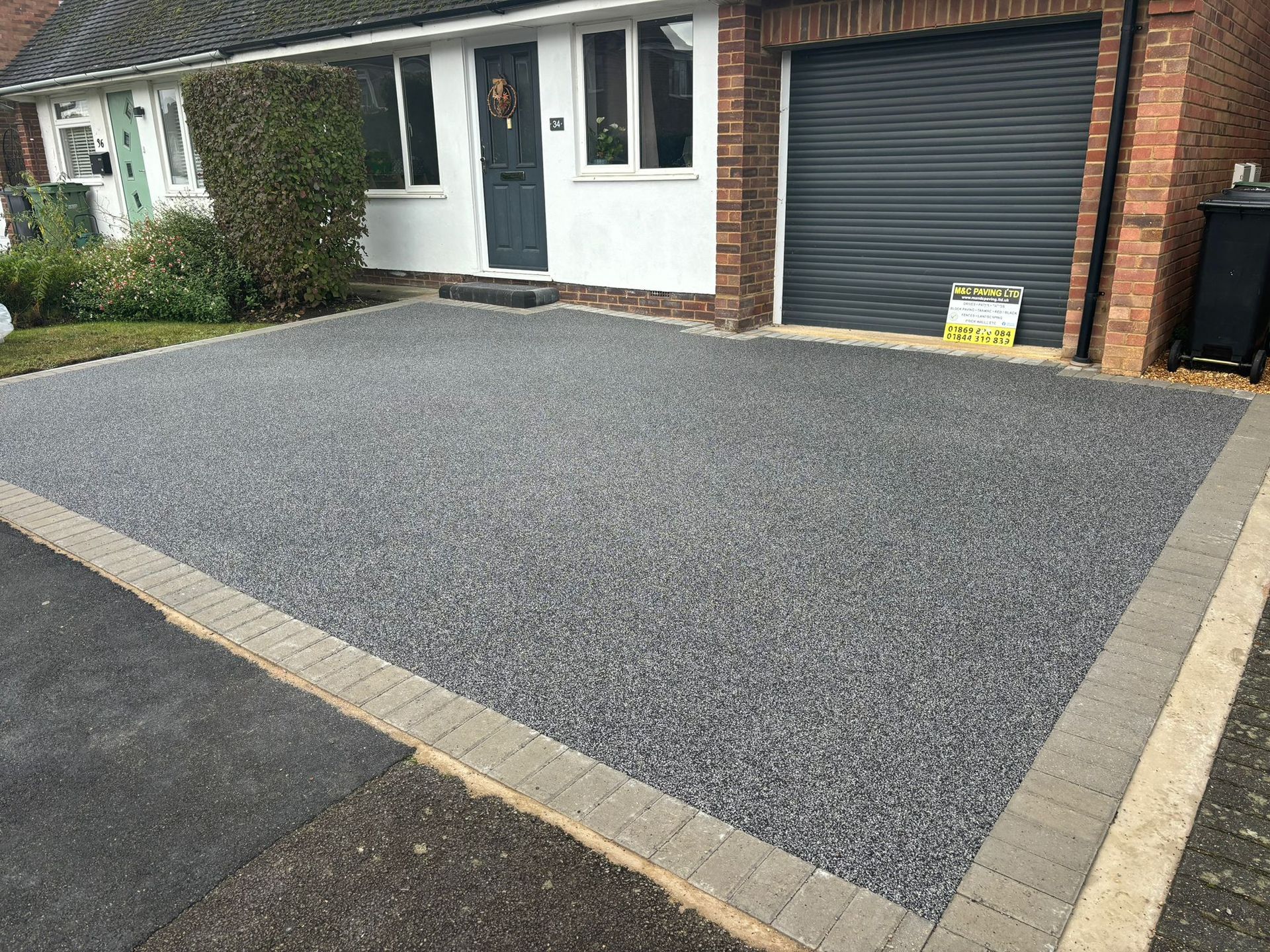 Newly resurfaced gray driveway beside a brick house with a garage door