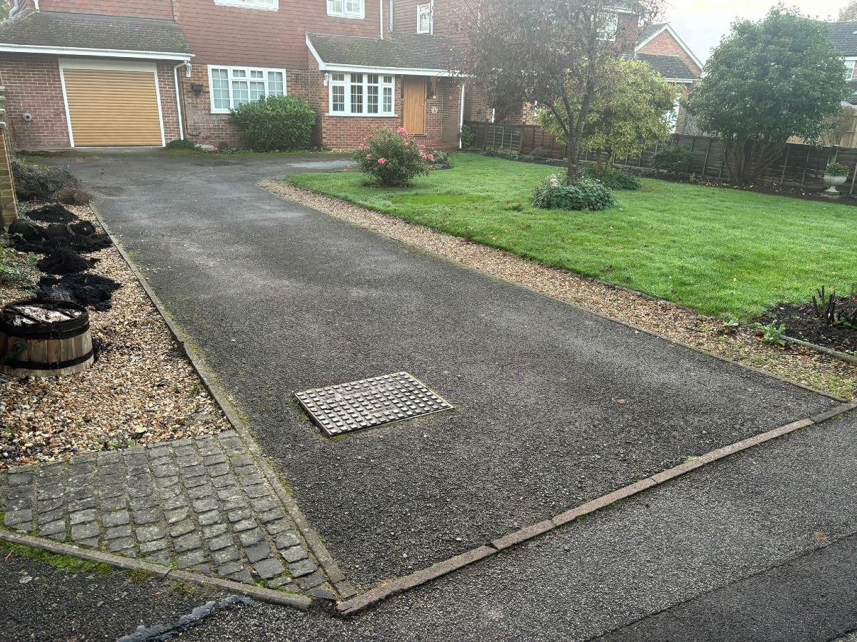 Driveway leading to a brick house with a green lawn and gravel border on a rainy day.