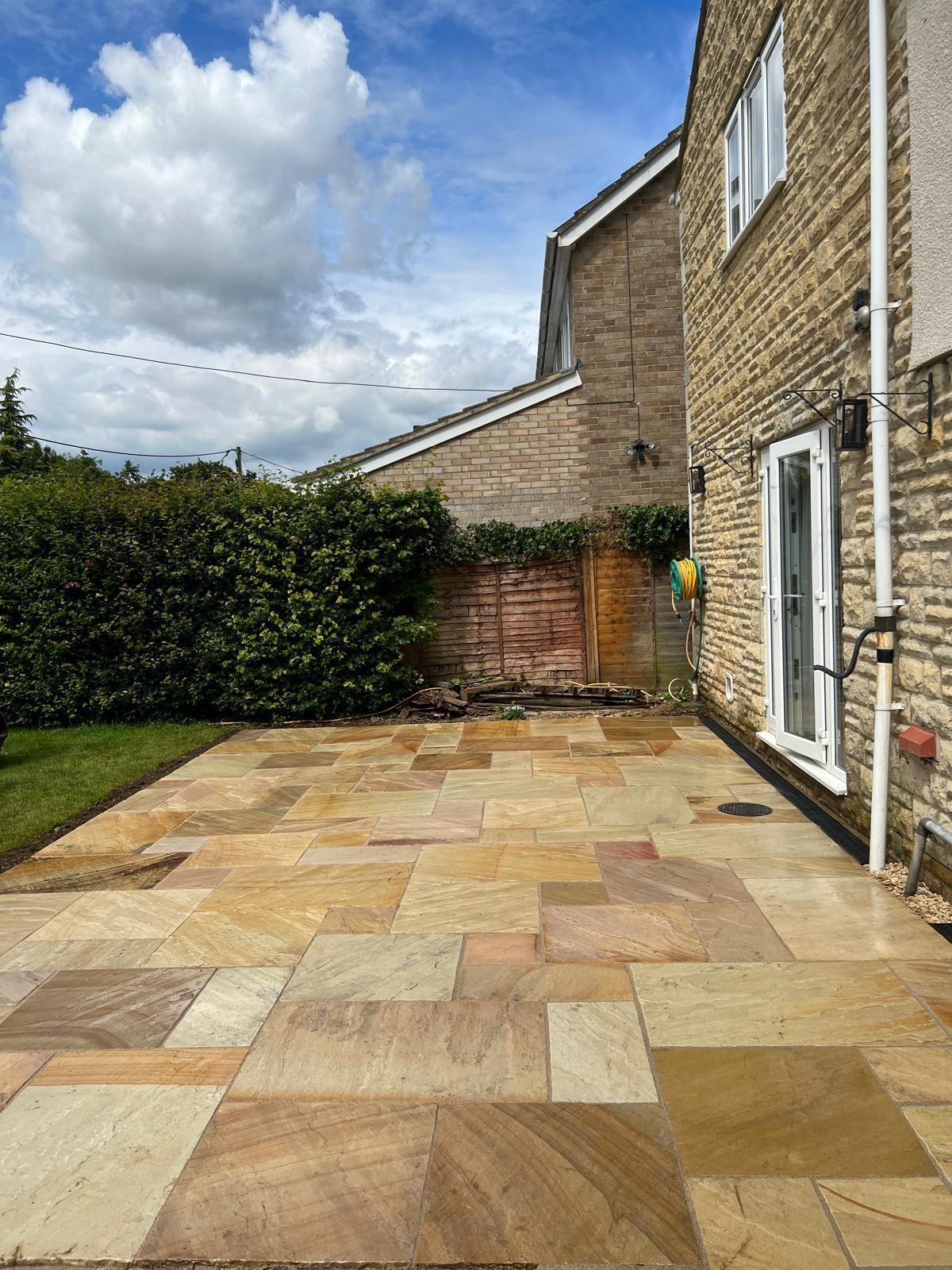 Stone patio beside a brick house and hedge under a cloudy sky