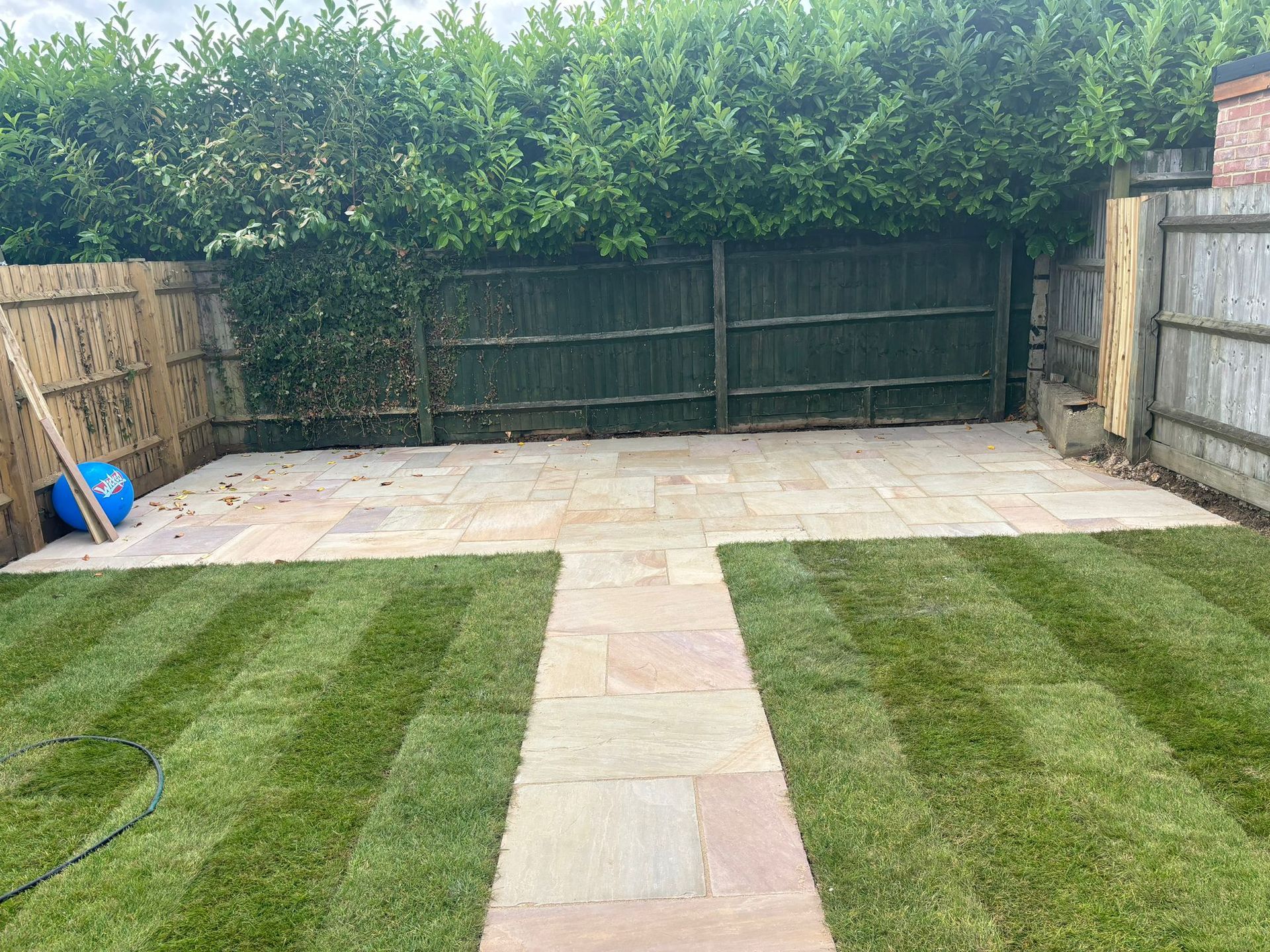 Backyard patio with striped lawn, central stone path, and a wooden fence gate at the far end