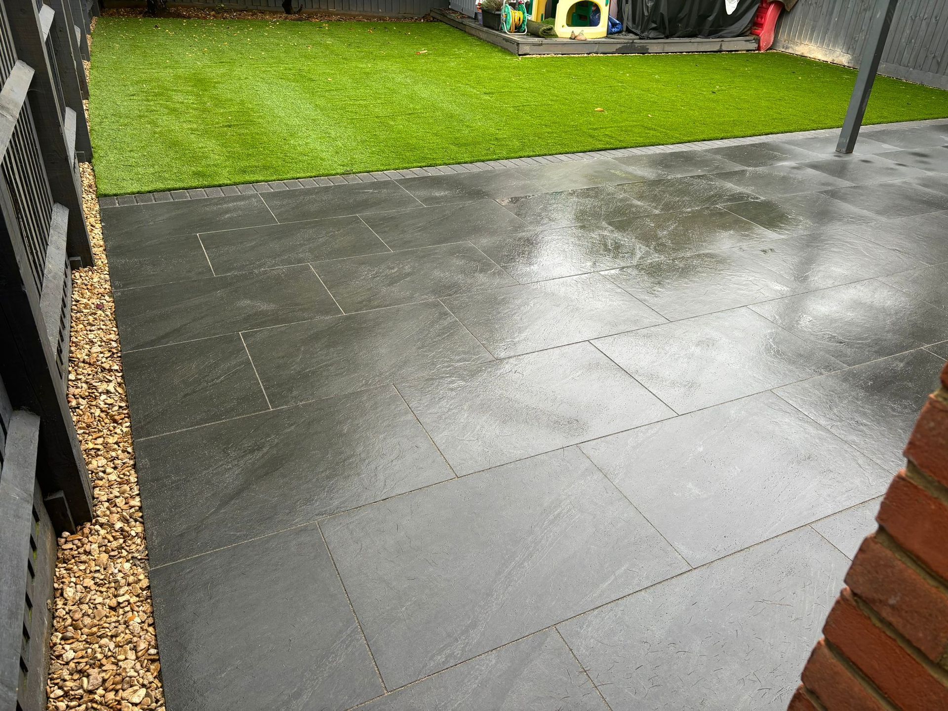 Rain-soaked patio tiles beside a bright green lawn and garden