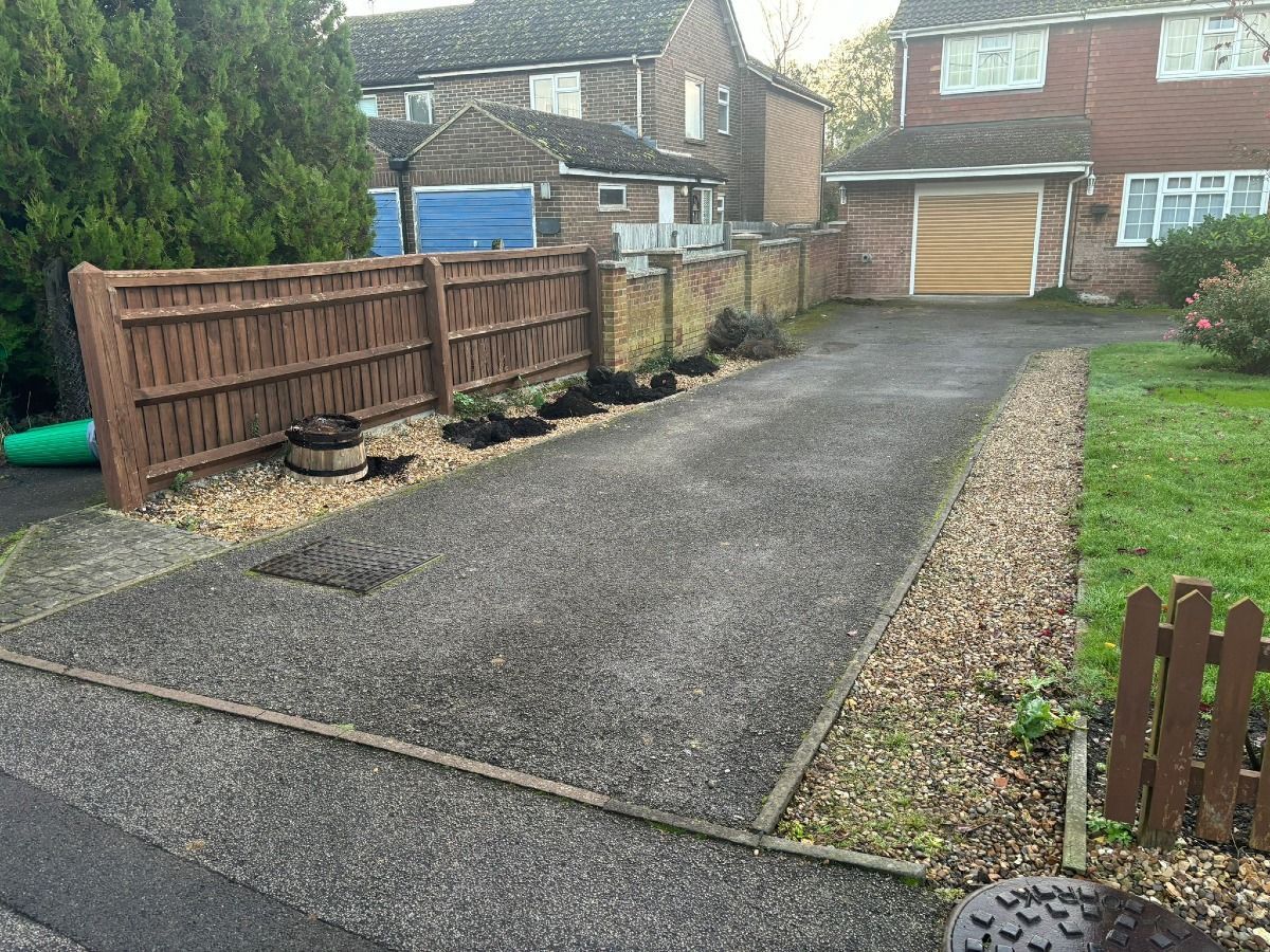 Residential driveway with wooden fence, gravel edges, and a garage in the background.