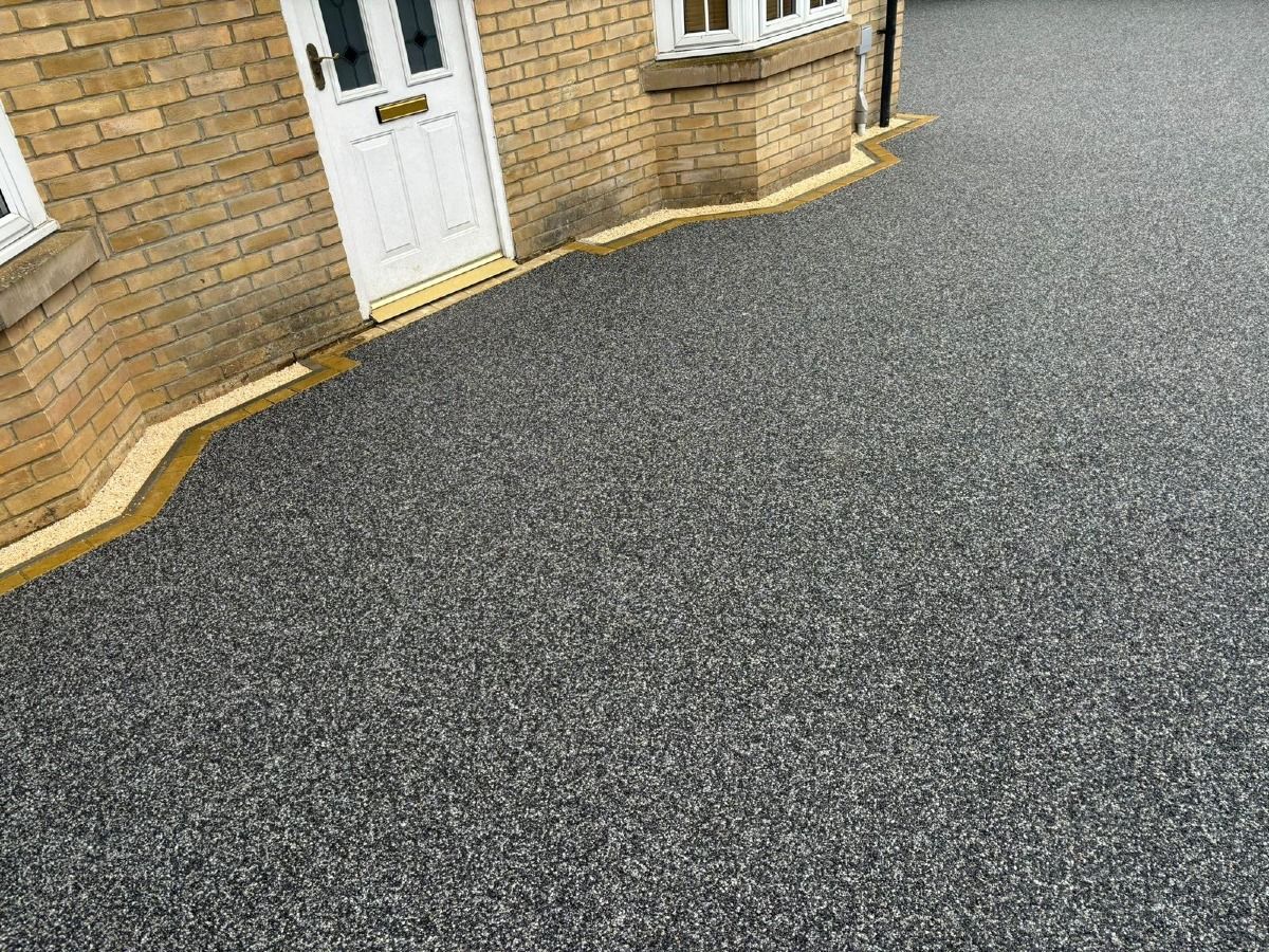 Brick building entrance with white door and large gray paved driveway.
