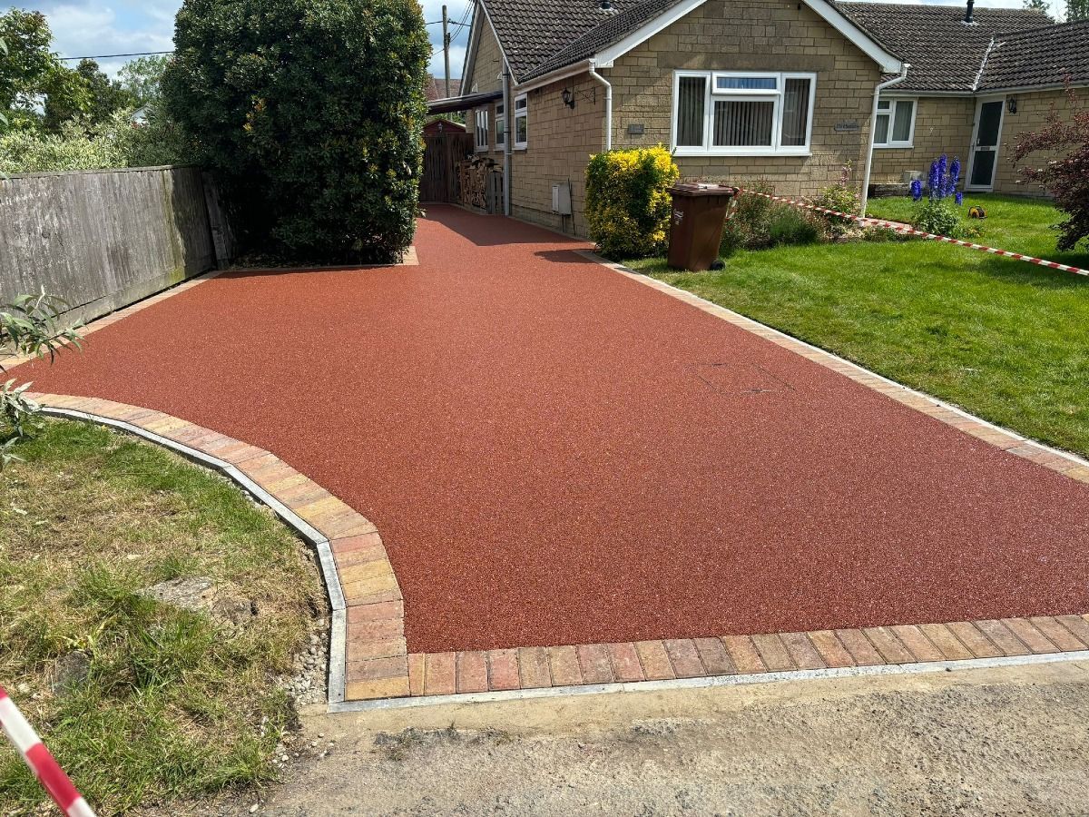 Red gravel driveway with brick border beside a house and lawn.