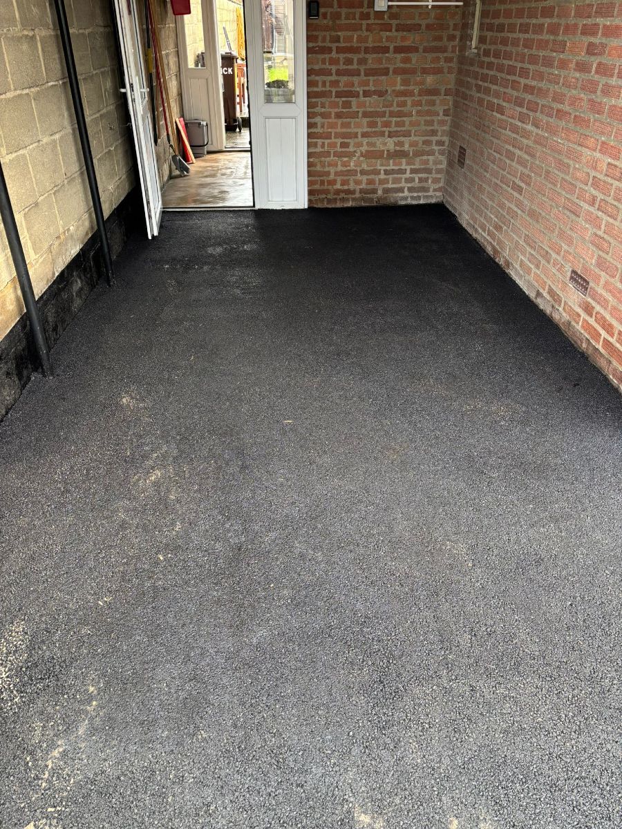 Narrow covered brick walkway with black carpeted floor and an open doorway at the end