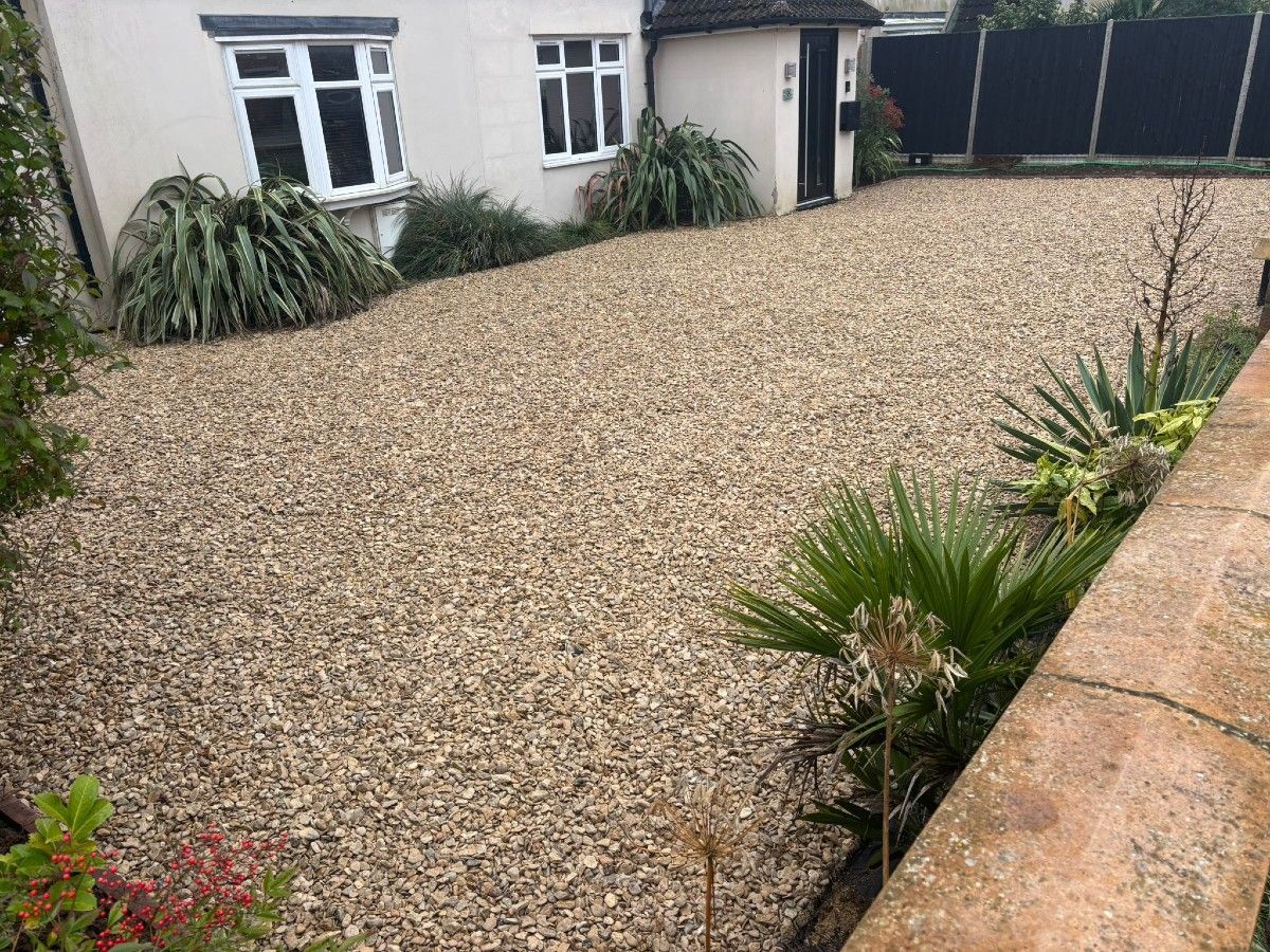 Gravel courtyard garden beside a white house with potted plants and a low stone wall