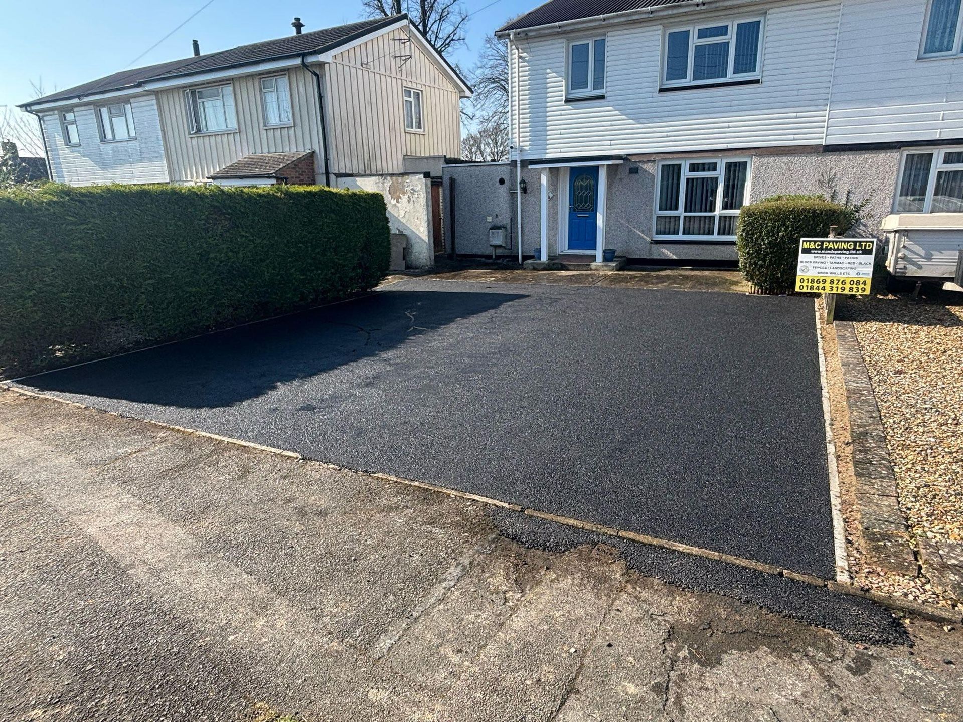 Residential driveway with fresh black asphalt leading to a two-story house and hedge-lined front yard