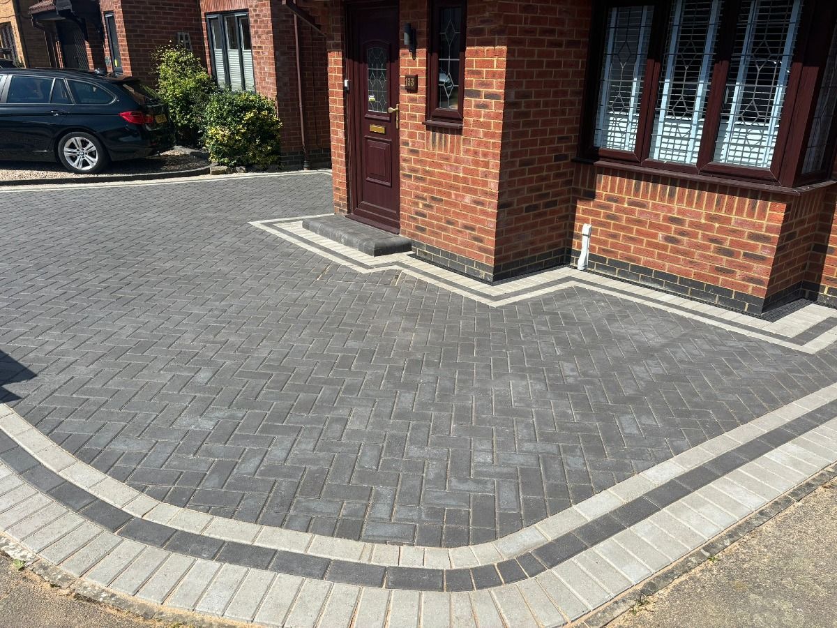 Paved brick driveway and walkway outside a red-brick building, with a parked car nearby.