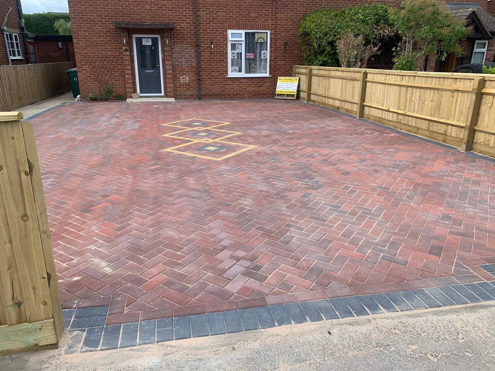 Empty brick-paved driveway with wooden fences and a brick house in the background
