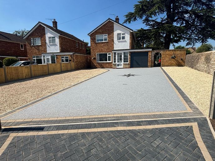 Detached brick house with a gravel driveway, garage, and front garden wall under a blue sky