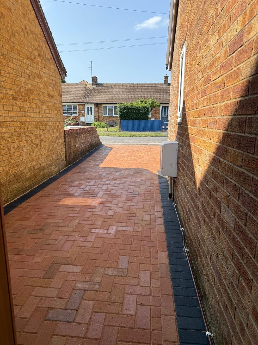Narrow brick-paved alley between brick walls leading to a sunny residential street.