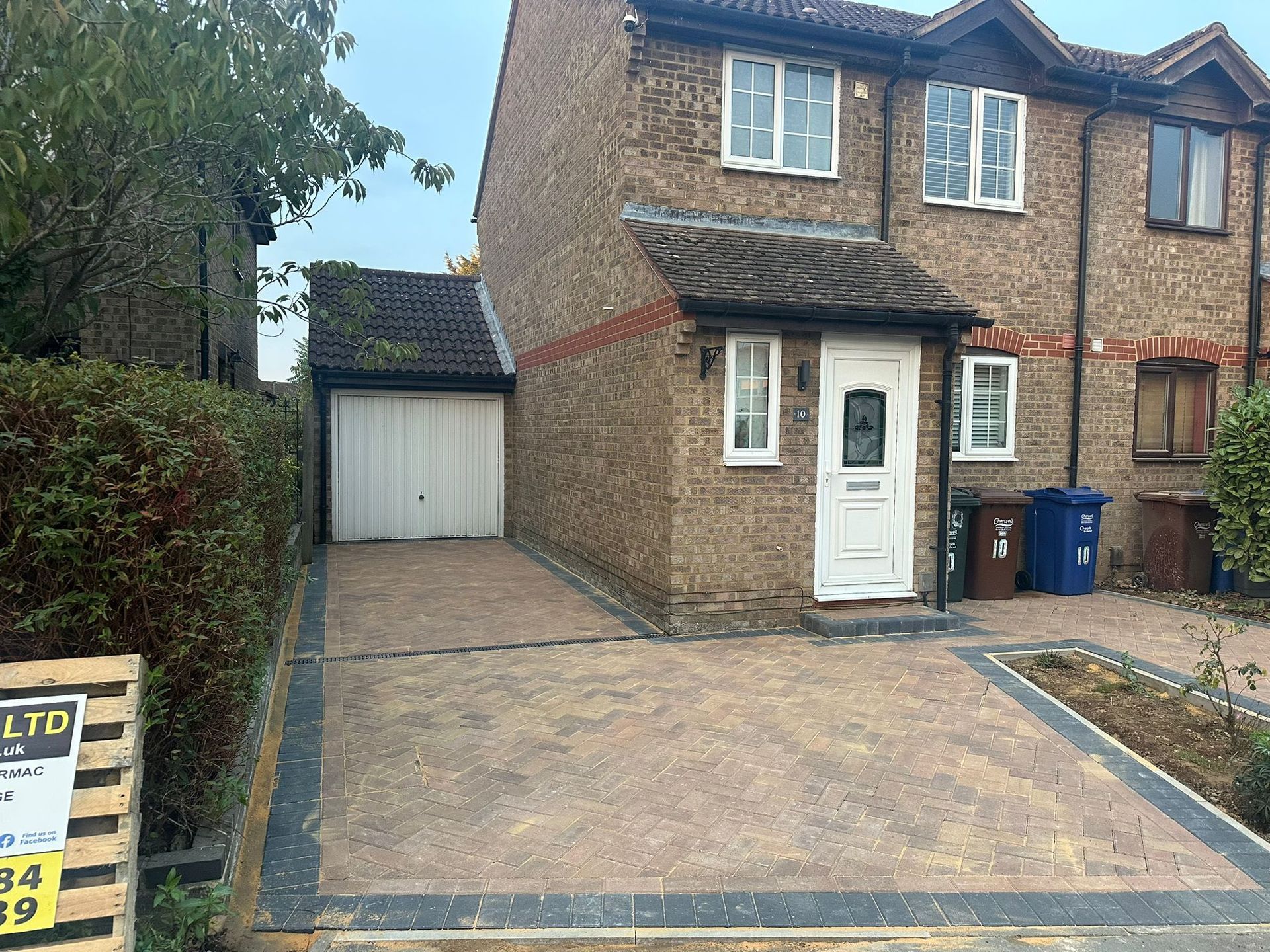 Brick semi-detached house with a white front door, garage, and paved driveway in a residential street