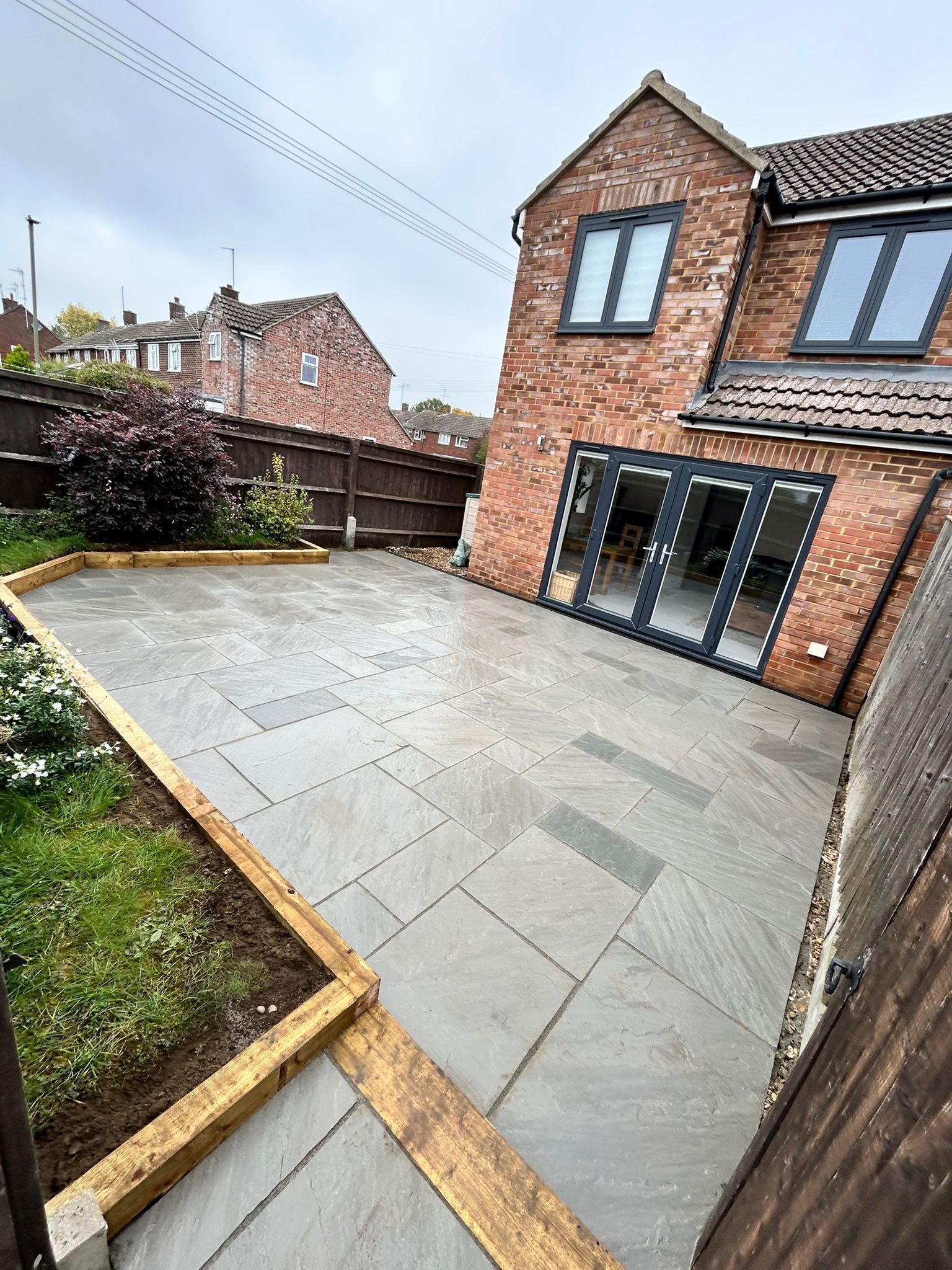 Brick house patio with large gray stone paving, raised planters, and sliding glass doors.
