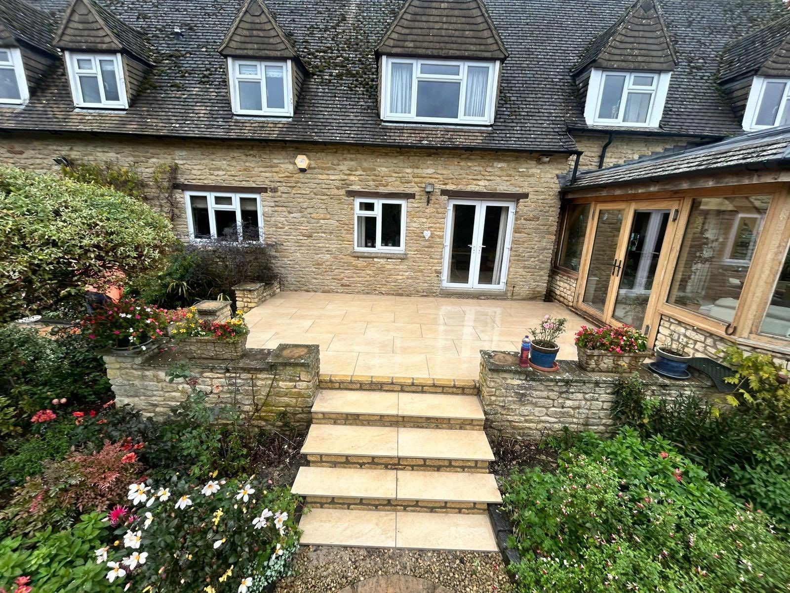 Stone cottage patio with steps, double doors, windows, and a flower-filled garden.
