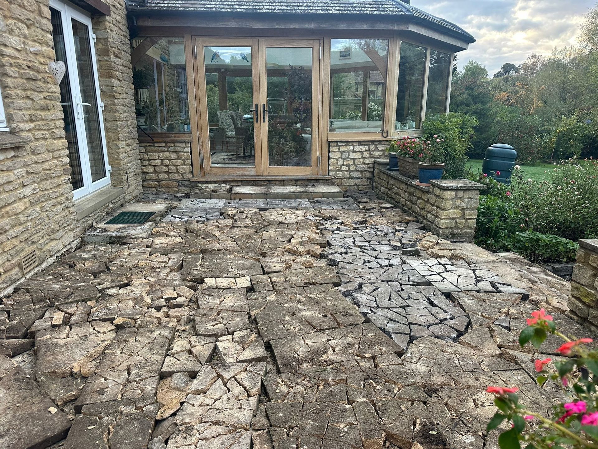 Stone patio and garden path leading to a house with glass doors, bordered by flowers and greenery.