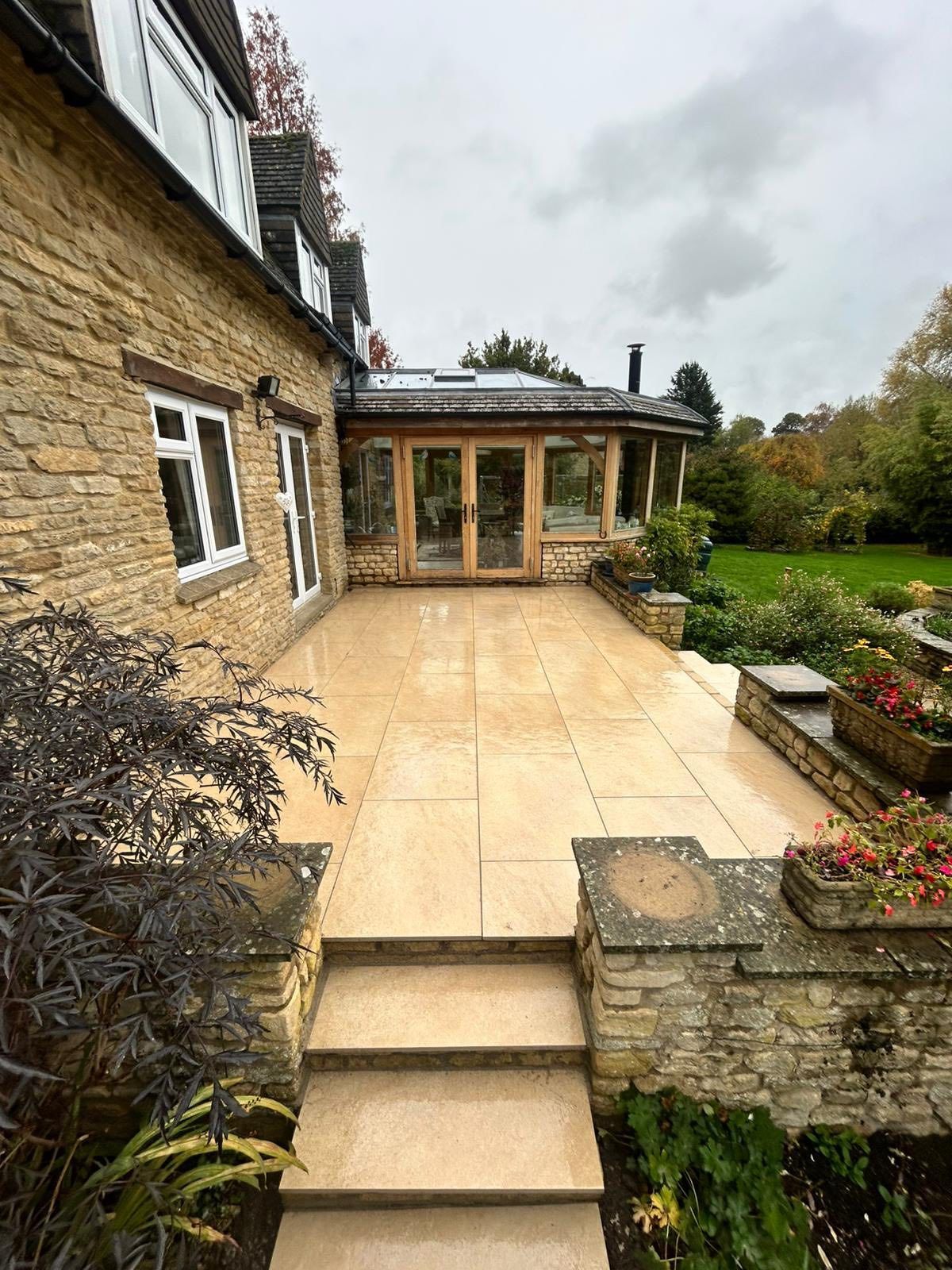 Stone patio steps leading to a glass conservatory beside a rustic house and garden