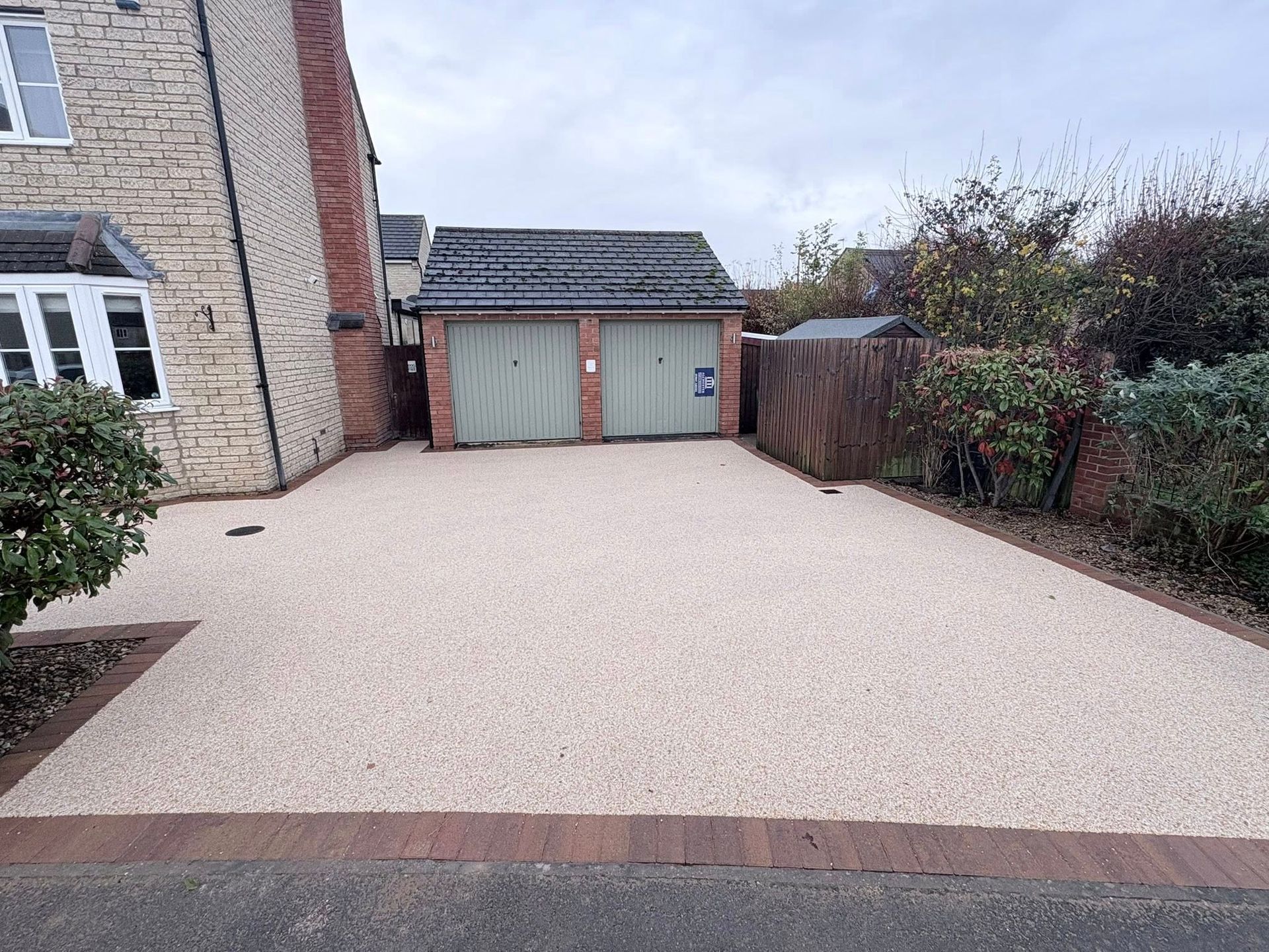 Gravel driveway beside a house, leading to a gray garage with double doors and hedges on the right