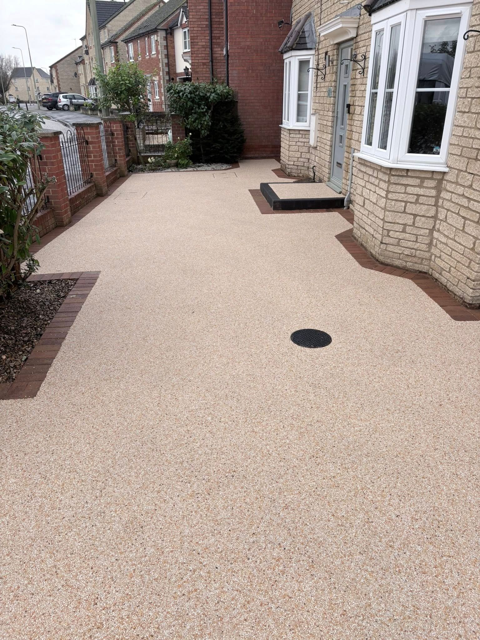 Front patio with beige resin driveway, brick house, bay window, and brick wall along the left side