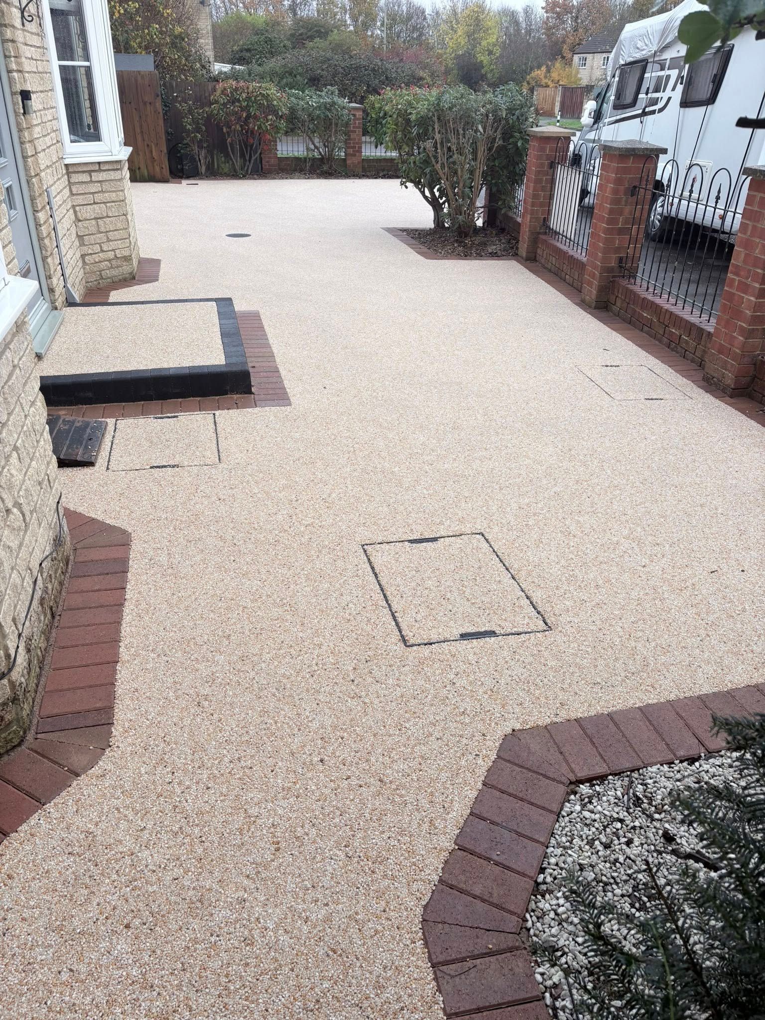 Gravel front yard path beside brick edging, a stone step, shrubs, and parked vans in the driveway